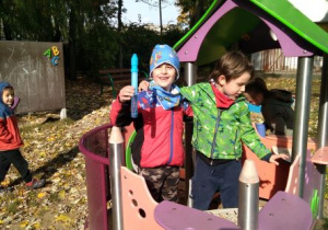 Chłopcy stoją w domku w ogrodzie przedszkolnym. Jeden z nich trzyma pojemnik z bańkami mydlanymi